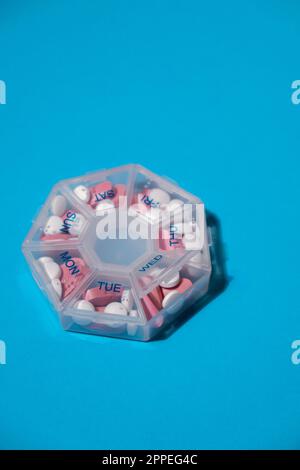 Organizer weekly shots on blue background with Copy space for your text. Closeup of medical pill box with doses of tablets for daily take medicine with white pink drugs and capsules. Daily vitamins at home. Medication dietary supplements, immunity and disease prevention Fish oil softgel, vitamin D and C omega minerals, fiber, fatty amino acids, probiotics sedatives. Health care and diseases cure Stock Photo