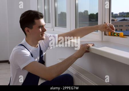 Worker using bubble level after plastic window installation indoors Stock Photo