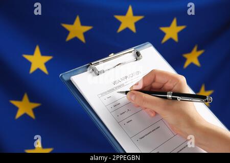 Woman filling visa application form against flag of European Union, closeup Stock Photo