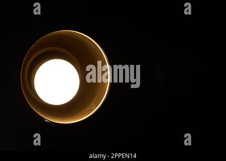 Yellowish light from a round bulb in a ceiling lamp with a black background helping new ideas or allowing illumination and leaving enough space for a text on the right Stock Photo