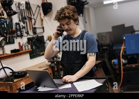 Blacksmith working with laptop and smartphone in his workshop Stock Photo