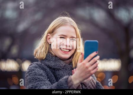 Smiling young woman using phone outdoors Stock Photo