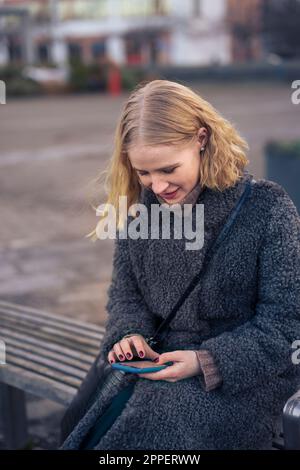 Young woman sitting on bench and using phone Stock Photo