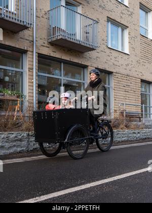Young mother cycling with two children in cargo bicycle Stock Photo