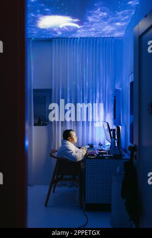 Boy at desk using computer at night Stock Photo