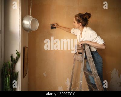 Woman on ladder scraping wall Stock Photo