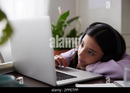 Girl doing homework with laptop at dining table Stock Photo