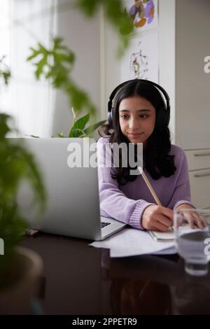 Girl doing homework with laptop at dining table Stock Photo