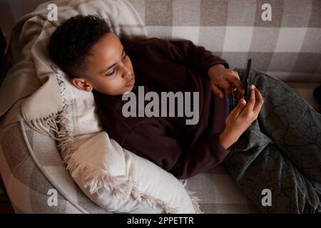 Boy lying on sofa and using phone Stock Photo