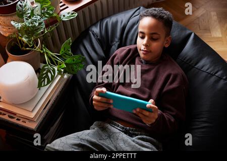 Boy lying on bean bag and playing video games Stock Photo