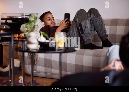 Boy lying on sofa and using phone Stock Photo
