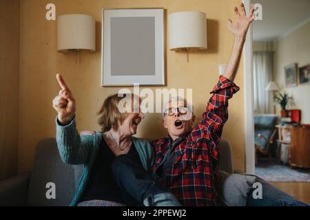 Senior couple sitting on sofa and singing Stock Photo