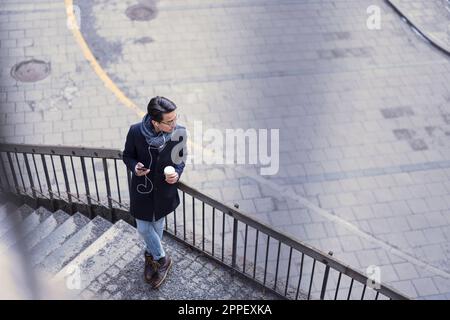 Handsome man with smartphone and paper cup standing on steps Stock Photo