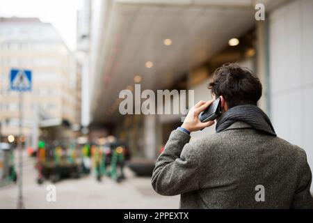 Rear view of man talking on phone in street Stock Photo