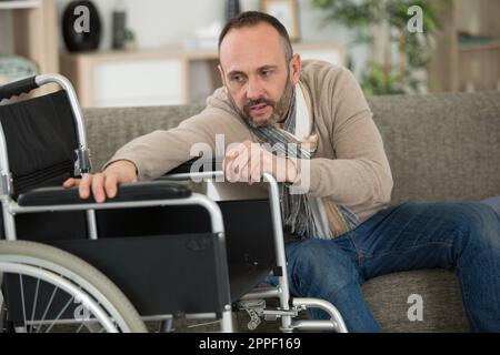 man trying to reach his wheelchair Stock Photo