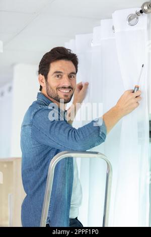 young man installing curtains over window Stock Photo