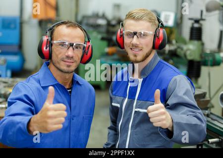 portrait of two engineers in machinery workshop holding thumbs up Stock Photo