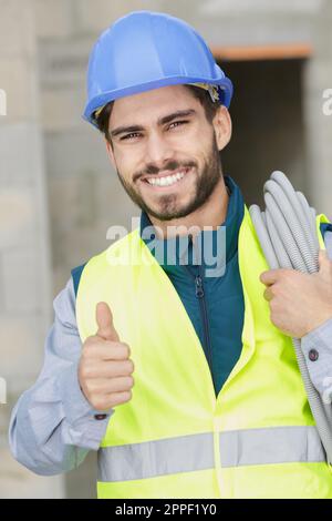 cheerful constructor with electric cable showing thumb up Stock Photo