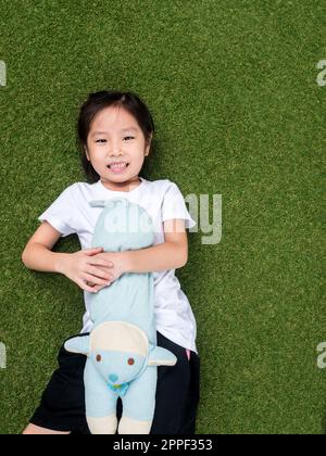 little asian kid girl lay down on the lawn with her doll Stock Photo