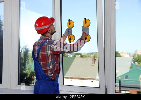 Worker using suction lifters during plastic window installation indoors Stock Photo