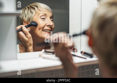 Mature woman is applying blush in the bathroom. Stock Photo