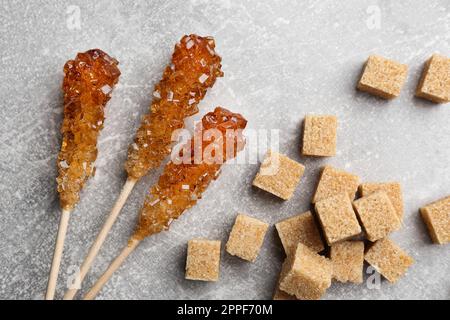 Wooden sticks with sugar crystals and cubes on light grey table, flat lay. Tasty rock candies Stock Photo