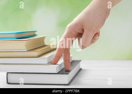 Man climbing up stairs of books with fingers on white wooden table against blurred background, closeup Stock Photo