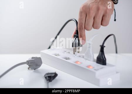 Closeup of a mans hand inserting a plug into electrical power strip. Stock Photo