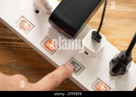 Close up a mans hand turn off the switch on power strip. Stock Photo