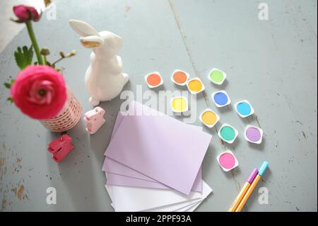 Lots of craft supplies on a wooden table. Paper, markers and colored leaves arranged on a table decorated with flowers and rabbits. Stock Photo