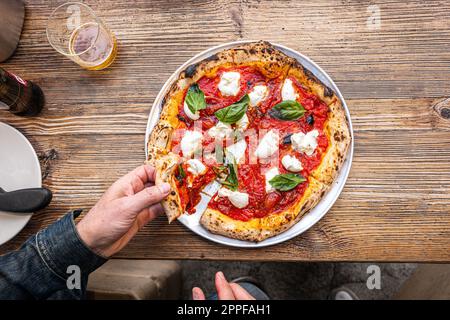 Neapolitan Margherita Pizza on a rustic wooden table in a traditional Pizzeria. Stock Photo