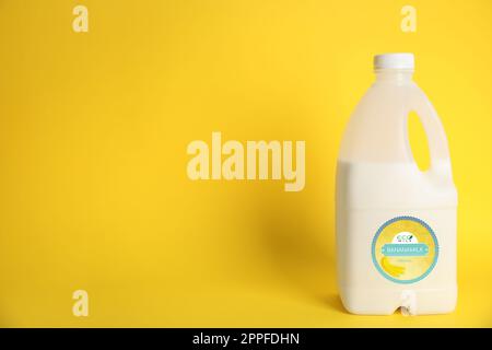 Gallon bottle of banana milk on yellow background, space for text. Vegan product Stock Photo
