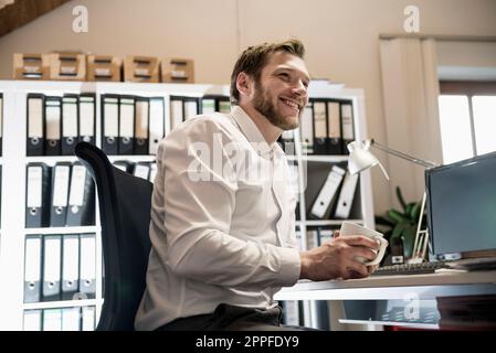 Mid adult businessman drinking coffee in an office and smiling, Bavaria, Germany Stock Photo