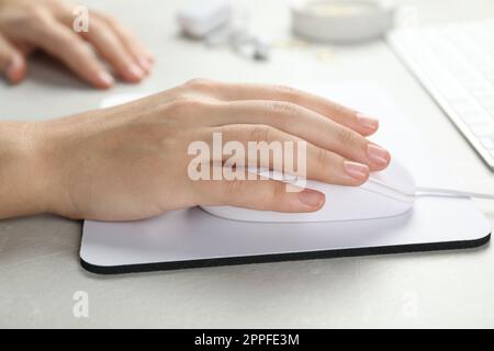 Woman using wired computer mouse on pad at light grey marble table, closeup Stock Photo