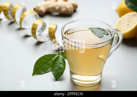 Herbal diet tea, lemon, ginger and measuring tape on light table Stock Photo