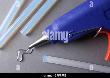 Blue glue gun and sticks on yellow background, flat lay Stock