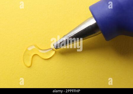 Melted glue dripping out of hot gun nozzle on yellow background, closeup Stock Photo