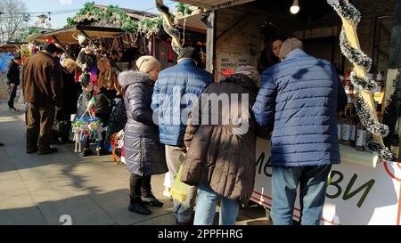 Belgrade, Serbia - January 24, 2020 People in warm jackets are looking at goods in a street shop. There are beautiful toys and wine in the shop window. Souvenir fair. Casual demi-season clothing Stock Photo