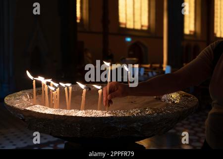 Worshiper lights candles that are placed on the edge of a baptismal font in Melbourne's St. Patrick's Cathedral. Atmospheric light Stock Photo