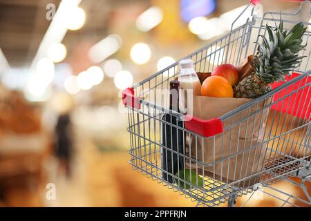 Shopping cart with different groceries in supermarket, space for text Stock Photo