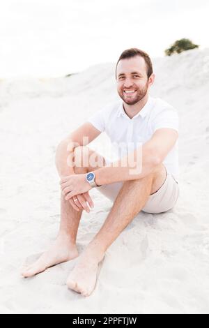 Young bearded happy man in light sitting on the beach Stock Photo
