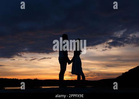 Couple standing holding hands at summer sunset Stock Photo