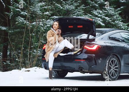Tired driver woman stopped her car in winter forest to give herself rest and to drink a cup of coffee Stock Photo