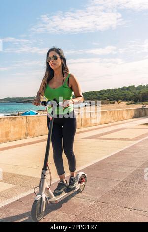 Woman riding electric scooter, happy and summer ride at tropical island beach resort for vacation. City, street and eco friendly transport, fun on escooter on holiday in mallorca,balearic island Stock Photo