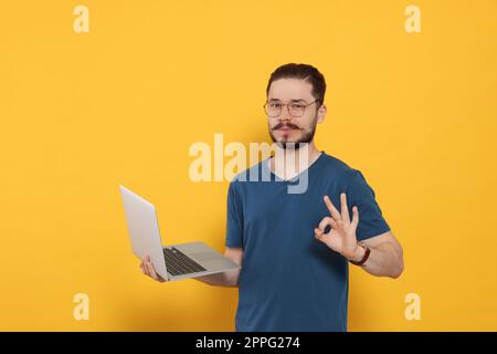 Handsome man with laptop showing OK gesture on orange background Stock Photo
