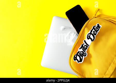 Different gadgets in bag with words DIGITAL DETOX on yellow background, flat lay. Space for text Stock Photo