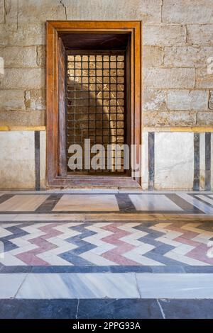 Recessed wooden window with decorated iron grid over stone bricks wall and decorative colorful floor Stock Photo