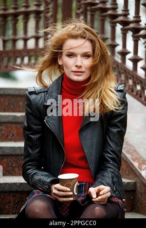 portrait of red hair lady in leather jacket with cardboard cup in hand Stock Photo