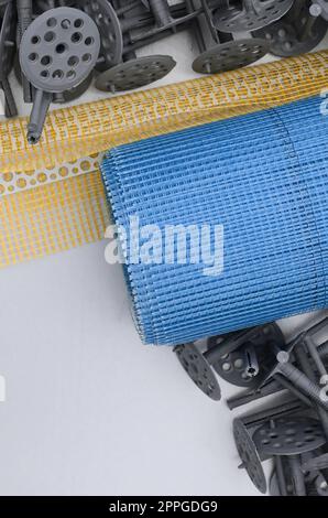 A set of construction items for the insulation of walls. Plastic dowels, a roll of mesh for the insulation of facades and a corner profile with a grid lie on the foam polystyrene surface Stock Photo