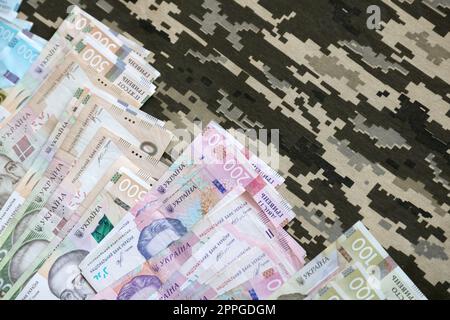 Ukrainian hryvnya bills on fabric with texture of Ukrainian military pixeled camouflage. Cloth with camo pattern in grey, brown and green pixel shapes Stock Photo